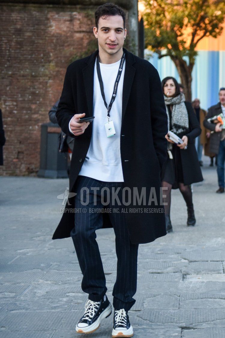 Men's winter/autumn coordinate and outfit with plain black chester coat, plain white sweatshirt, navy striped slacks, and Converse All Star JW Anderson black high-cut sneakers.