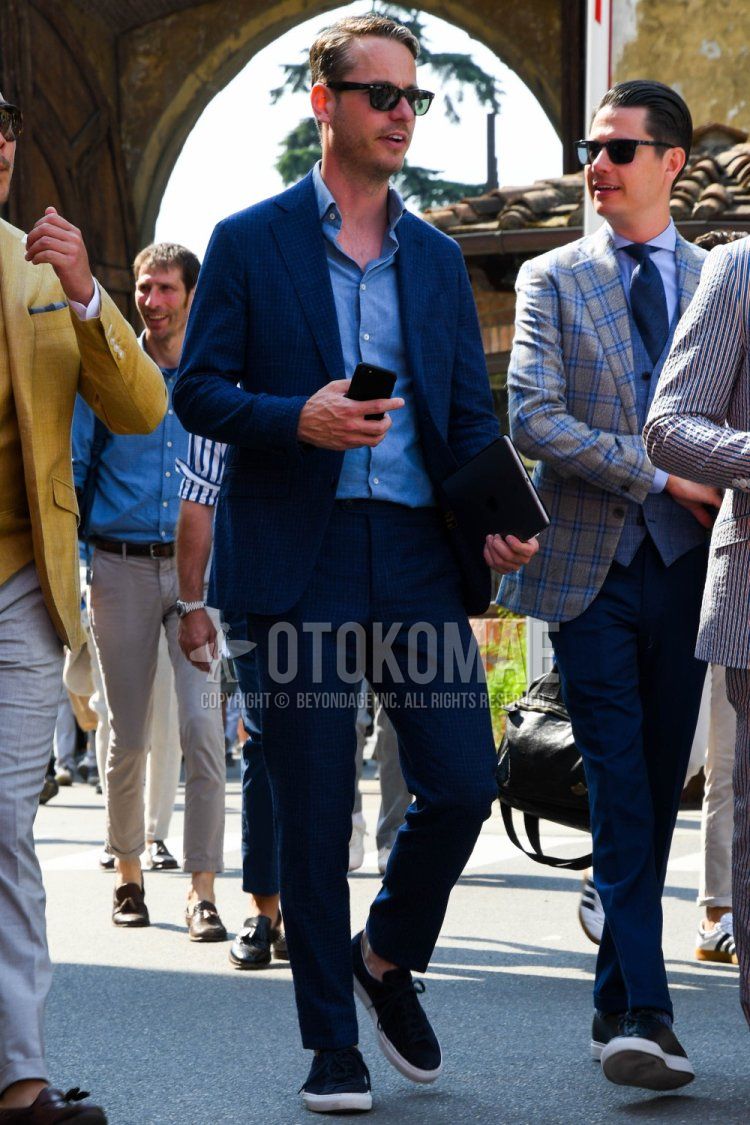 Men's spring, summer, and fall coordinate and outfit with Ray-Ban Wayfarer Wellington plain black sunglasses, plain blue shirt, black low-cut sneakers, and navy check suit.