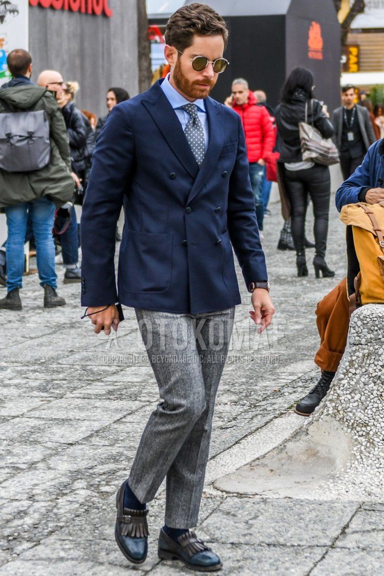 Winter men's coordinate and outfit with solid color sunglasses, solid color navy tailored jacket, solid color light blue shirt, solid color gray slacks, solid color navy socks, navy loafer leather shoes and gray dot tie.