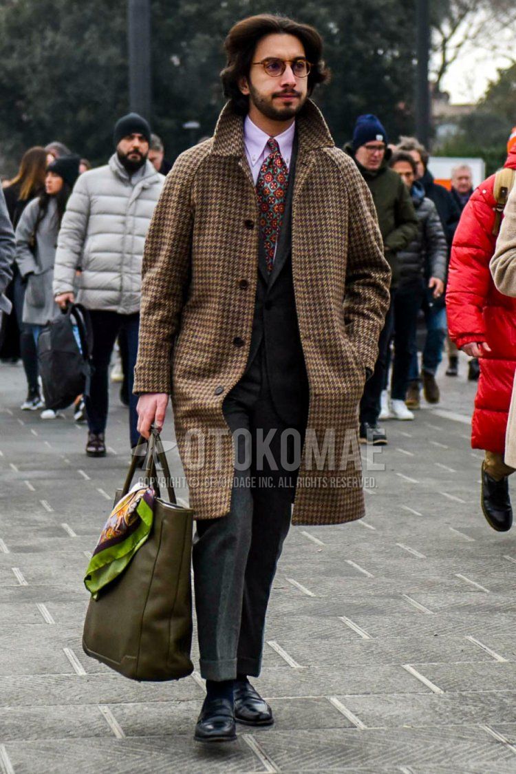 Winter men's coordinate and outfit with brown tortoiseshell glasses, brown checked stainless coat, solid pink shirt, solid black socks, black coin loafer leather shoes, solid olive green tote bag, solid gray suit, and multi-colored tie.