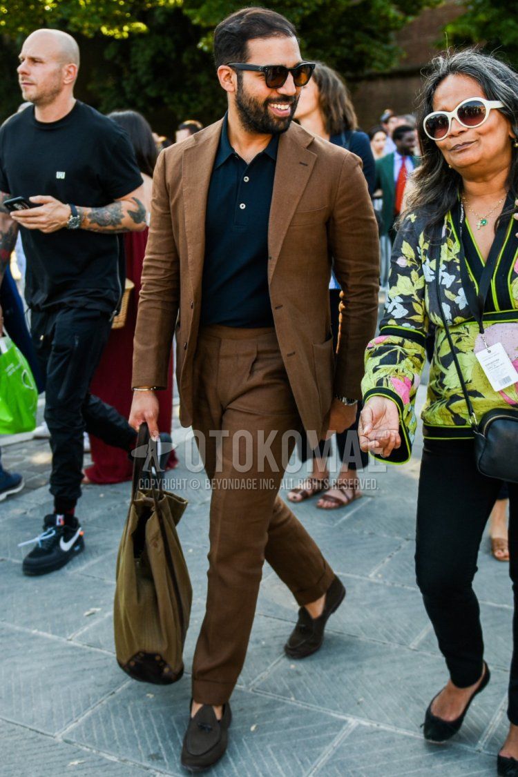 Men's spring/summer/fall outfit with plain black sunglasses, plain black polo shirt, suede brown loafer leather shoes, plain brown tote bag, and plain brown suit.