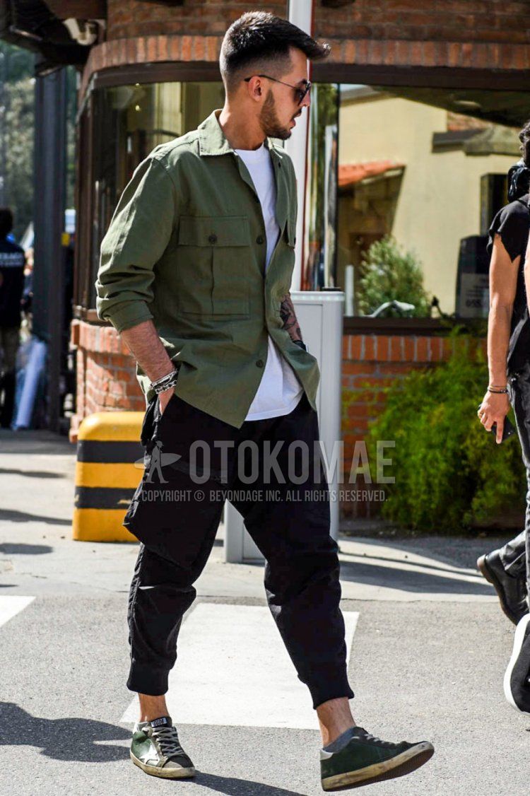 Men's spring, summer, and fall coordinate and outfit with olive green solid color safari jacket, white solid color t-shirt, black solid color cargo pants, and green low-cut sneakers by Golden Goose.