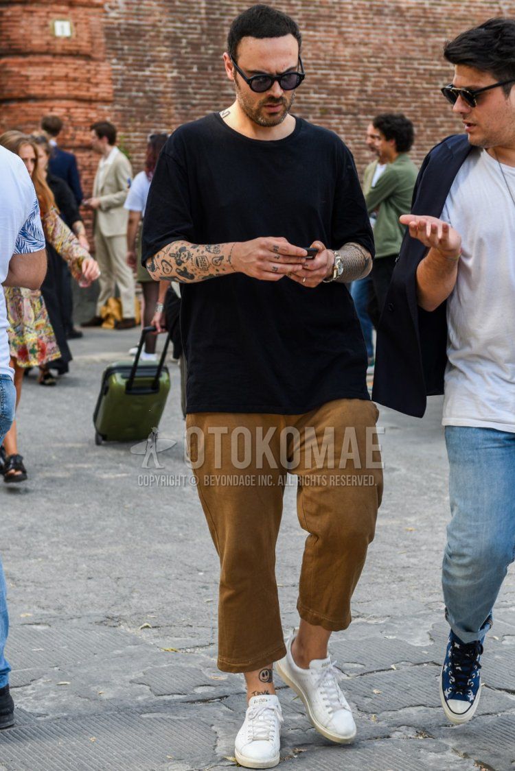 黒無地のサングラス、黒無地のTシャツ、ブラウン無地のチノパン、無地のクロップドパンツ、白ローカットのスニーカーを合わせた夏のメンズコーデ・着こなし。