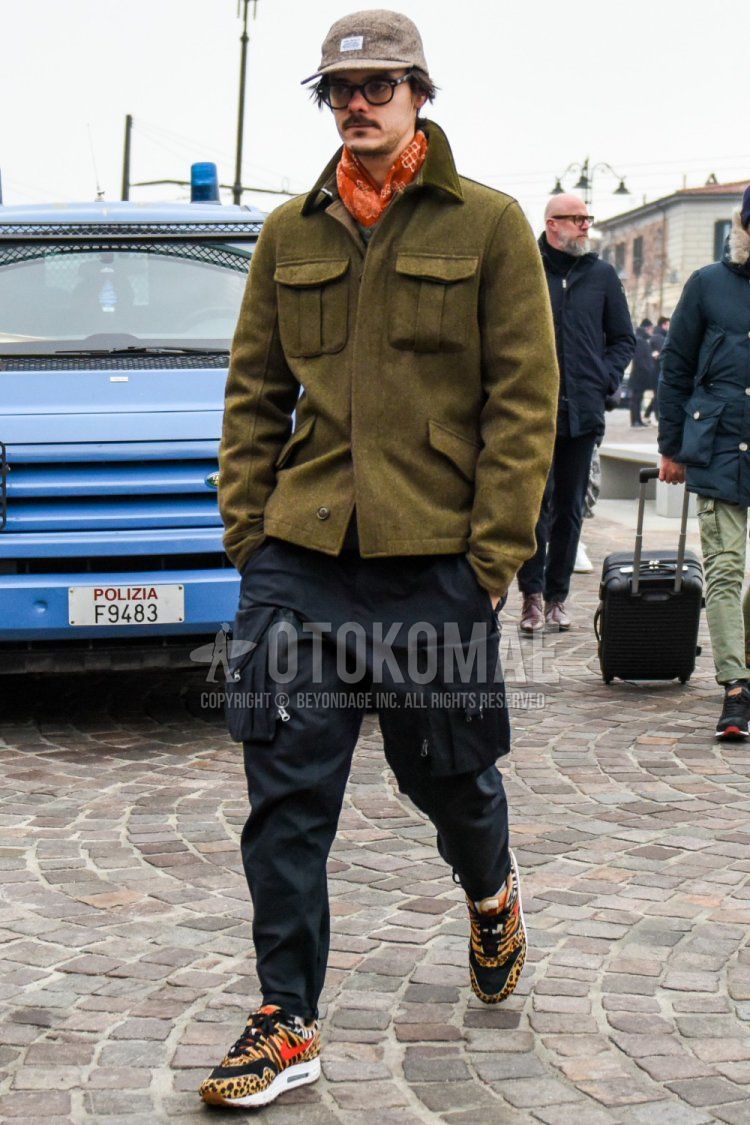 Men's fall/winter coordinate and outfit with solid beige baseball cap, solid black glasses, orange scarf/stall, solid olive green shirt jacket, solid black cargo pants, and Nike Atmos Air Max 1 black/beige low-cut sneakers.