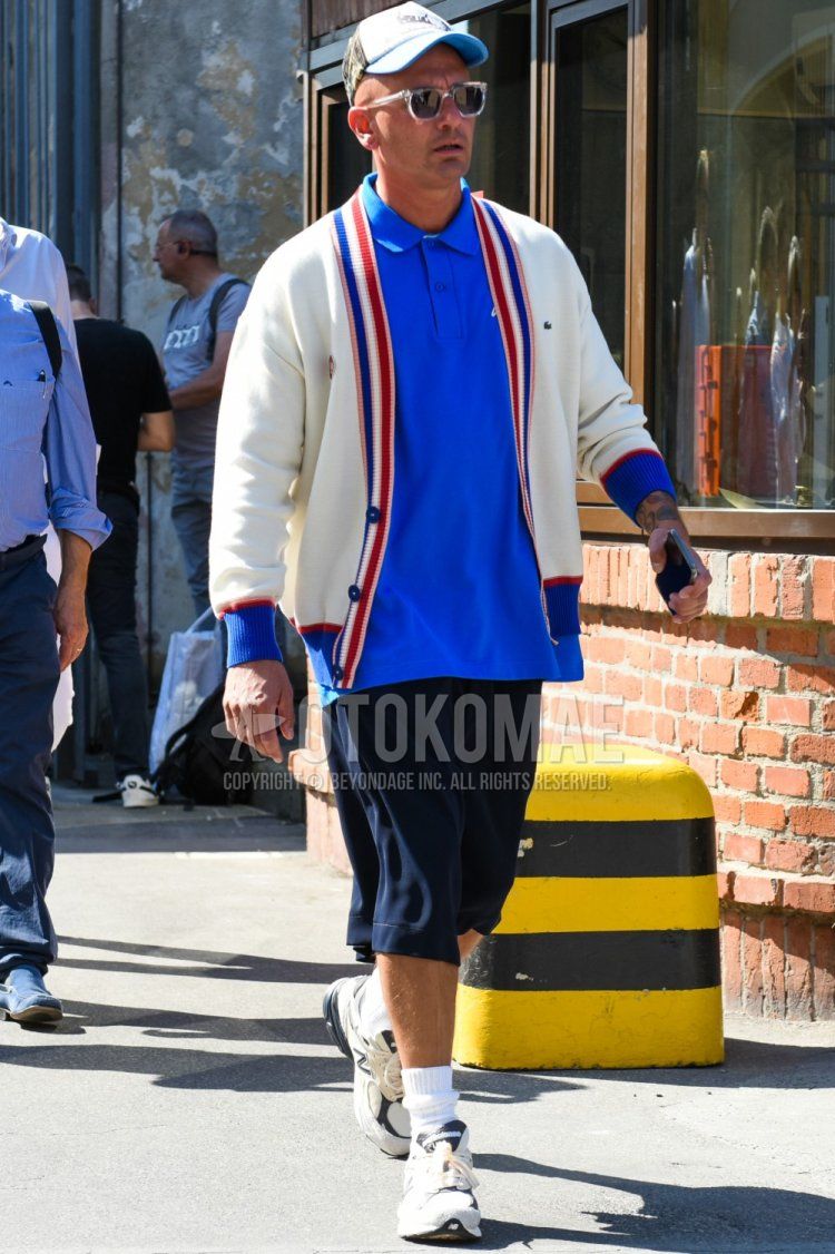 Men's spring/summer coordinate and outfit with light blue/white camouflage baseball cap, clear solid color sunglasses, solid white cardigan, solid blue polo shirt, solid navy shorts, solid white socks, and white sneakers.