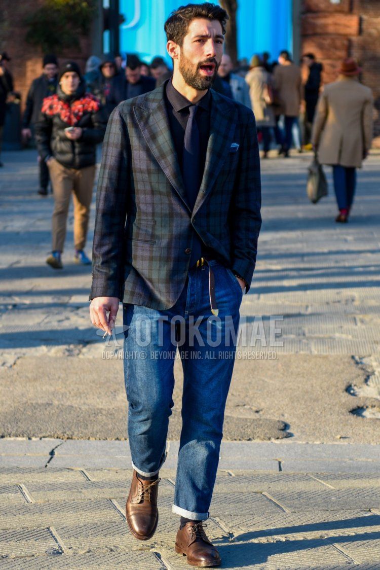 Men's fall/winter outfit with olive green/navy check tailored jacket, solid black shirt, solid brown leather belt, solid blue denim/jeans, solid navy socks, brown straight tip leather shoes and solid navy tie.