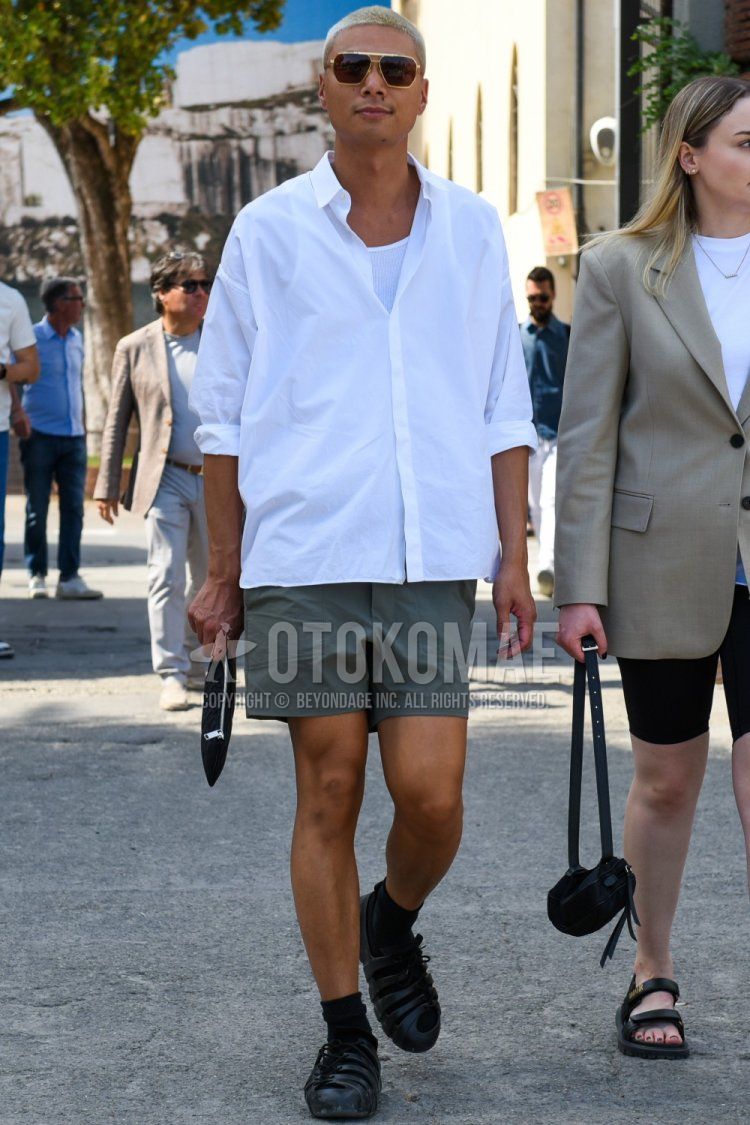 Men's spring/summer coordinate and outfit with solid gold sunglasses, solid white shirt, solid white tank top, solid olive green shorts, solid black socks, black sports sandals, solid black clutch/second bag/drawstring bag.