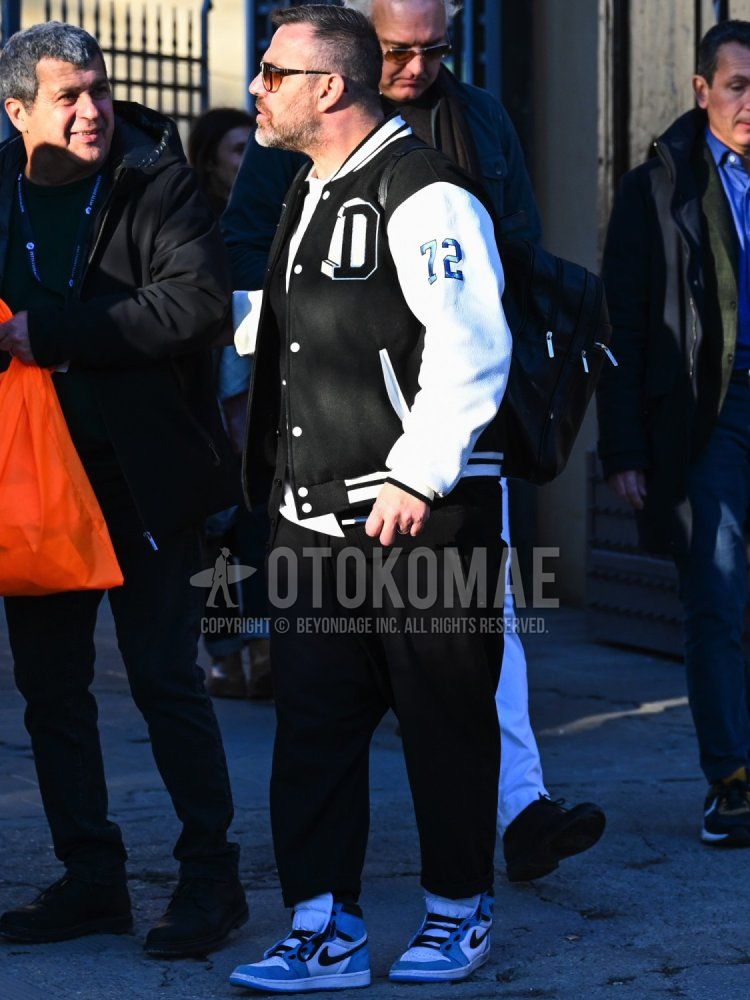Men's spring/fall/winter coordinate and outfit with plain black stadium jacket, plain white long T, plain black cardigan, plain black wide pants, blue, white, and black high-cut sneakers, and plain black backpack.