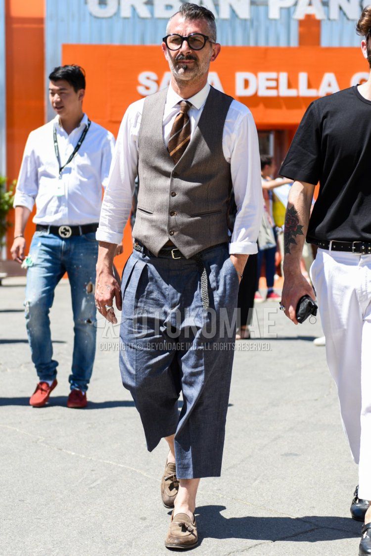 Men's spring/summer/fall outfit with plain black glasses, plain white shirt, plain gray gilet, plain black mesh belt, plain black leather belt, plain gray cropped pants, plain gray slacks, suede beige tassel loafer leather shoes, and brown regimental tie. Outfit.