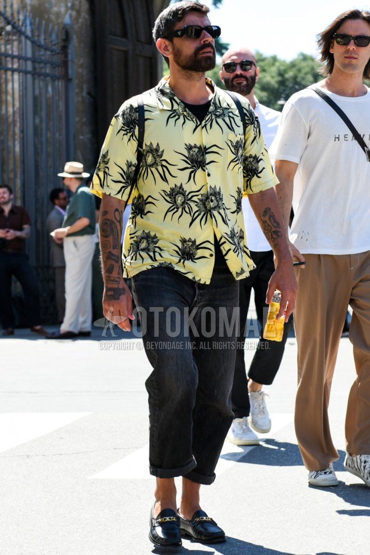 Men's spring/summer coordinate and outfit with plain black sunglasses, yellow botanical shirt, plain black t-shirt, plain black denim/jeans, plain black bit loafer leather shoes, and plain black backpack.