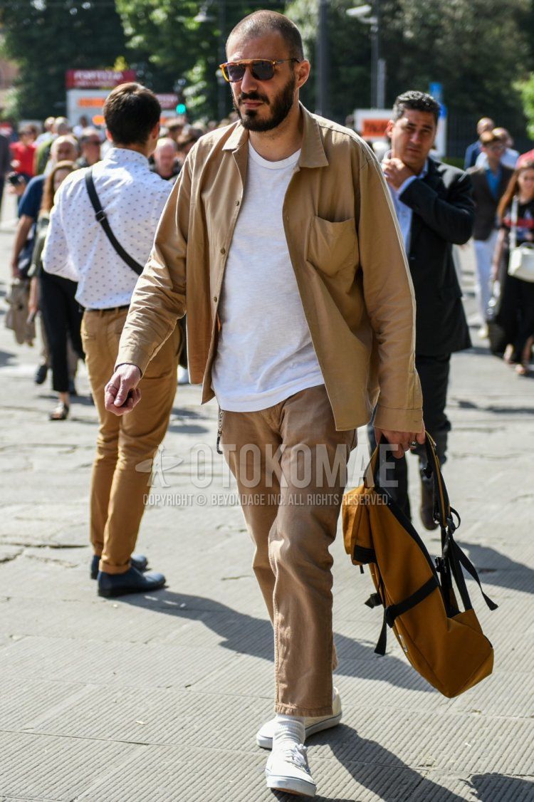 Men's spring and fall outfit with brown tortoiseshell sunglasses, plain beige shirt jacket, plain white t-shirt, plain beige cotton pants, plain white socks, white low-cut sneakers by Vans, and yellow bag backpack.