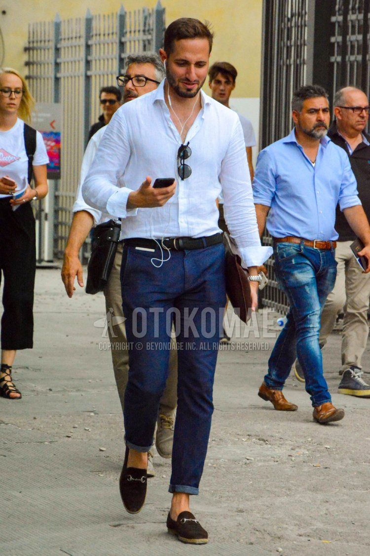 Men's spring/summer/fall outfit with plain white shirt, plain navy leather belt, plain navy denim/jeans, brown bit loafer leather shoes, plain brown clutch/second bag/drawstring bag.