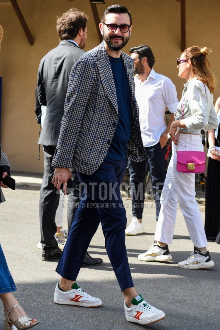 Men's spring, summer, and fall coordination and outfit with plain black/red sunglasses, navy/gray checked tailored jacket, plain navy t-shirt, plain navy ankle pants, and white low-cut sneakers.
