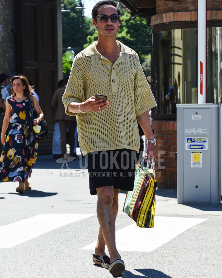 Men's summer/spring outfit with plain gray sunglasses, plain yellow polo shirt, solid black shorts, solid black espadrilles, and yellow striped briefcase/handbag.
