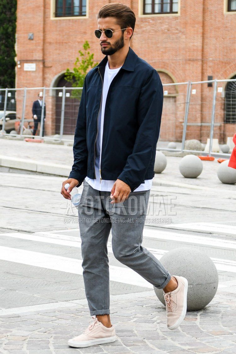 Men's spring and fall outfit with plain sunglasses, plain navy shirt jacket, plain white t-shirt, plain gray easy pants, and Vans Old Skool pink low-cut sneakers.