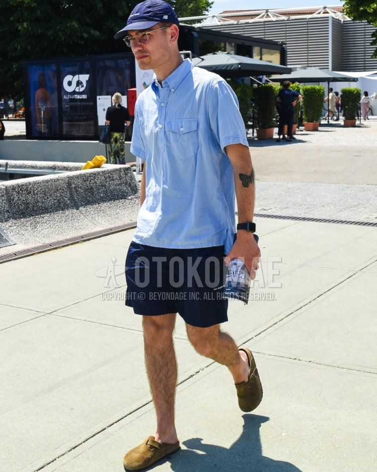 Men's spring/summer coordinate and outfit with navy one-point baseball cap, gold eyewear glasses, plain blue shirt, plain navy shorts, and Birkenstock Boston brown leather sandals.