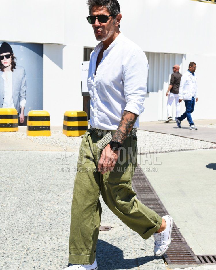 Summer/spring men's coordinate and outfit with plain black sunglasses, plain white shirt, plain white leather belt, plain olive green baker pants, and white low-cut Converse sneakers.