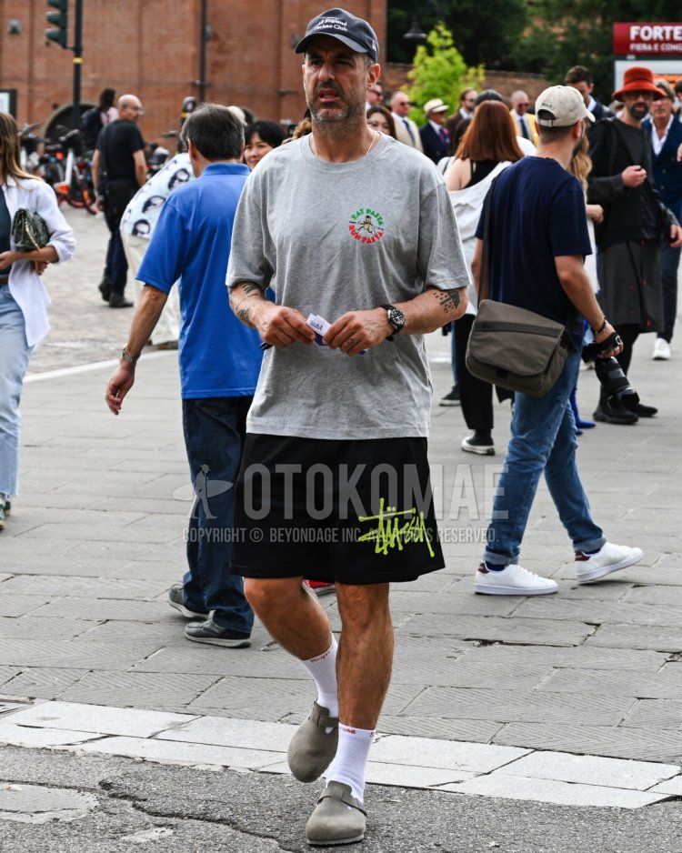 Men's spring/summer coordinate and outfit with gray one-point baseball cap, gray one-point T-shirt, Stussy black decal logo shorts, plain white socks, and Birkenstock beige leather sandals.