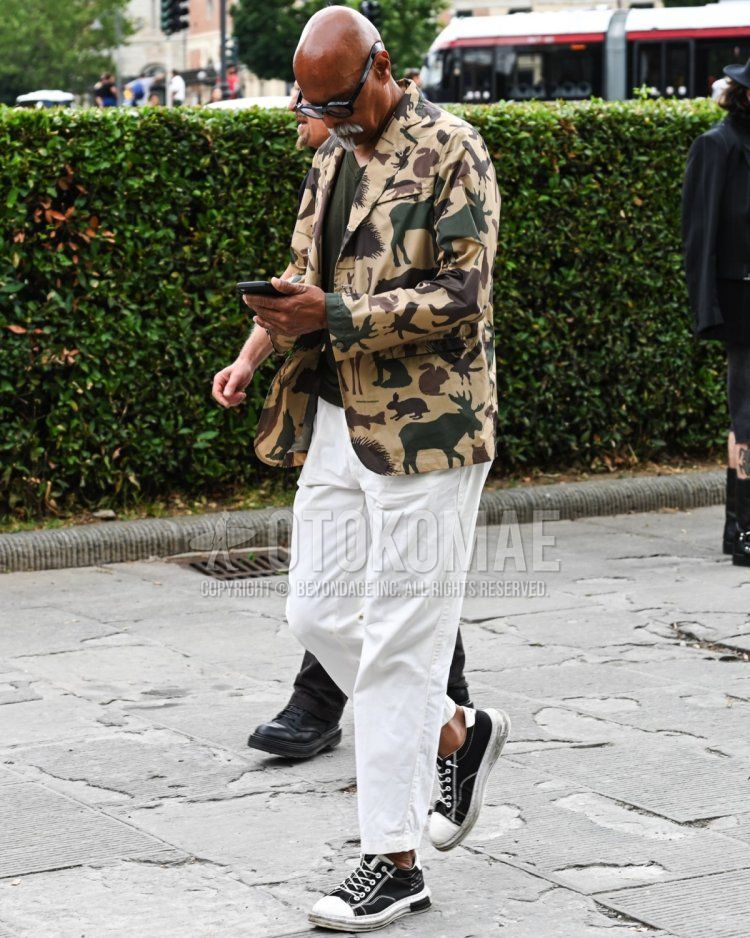 Men's spring, summer, and fall coordinate and outfit with plain black sunglasses, beige camouflage tailored jacket, plain olive green t-shirt, plain white chinos, and black low-cut sneakers.