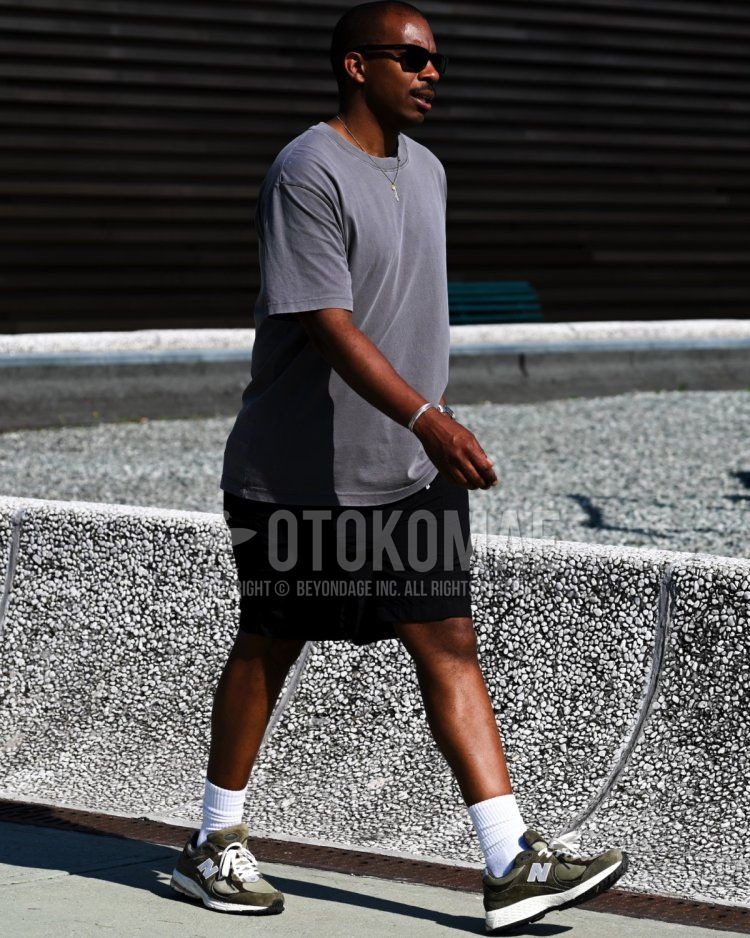 Summer/spring men's coordinate and outfit with plain black sunglasses, plain gray t-shirt, plain black shorts, plain light blue socks, and New Balance green low-cut sneakers.