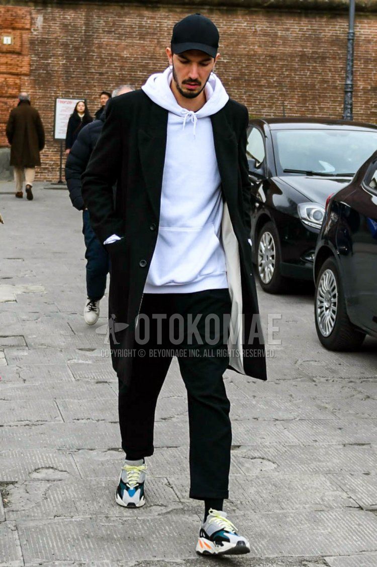 Men's fall/winter coordinate and outfit with plain black baseball cap, plain black chester coat, plain white hoodie, plain black slacks, plain black cropped pants, plain black socks, and Adidas Yeezy Boost 700 gray low-cut sneakers.