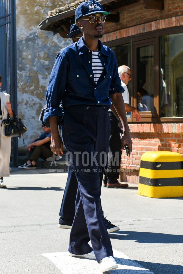 Men's spring/summer coordinate and outfit with plain navy baseball cap, plain gold sunglasses, plain navy shirt, white striped t-shirt, plain navy slacks, and white low-cut sneakers.