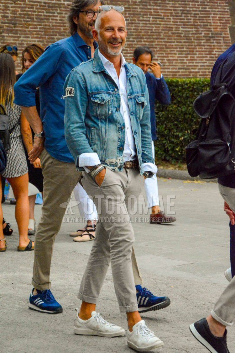 Spring and fall men's coordinate and outfit with clear solid sunglasses, blue solid denim jacket, white solid shirt, brown solid leather belt, beige solid chinos and white low-cut Golden Goose sneakers.