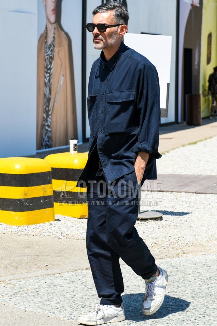 Summer/spring men's coordinate and outfit with plain black sunglasses, plain navy shirt, plain black t-shirt, plain blue chinos, and white low-cut sneakers.