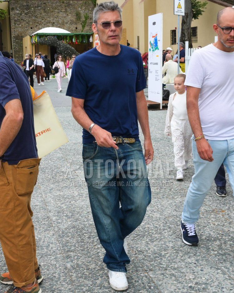Men's spring/summer coordinate and outfit with solid black sunglasses, solid navy t-shirt, solid beige mesh belt, solid blue denim/jeans, and white low-cut sneakers.