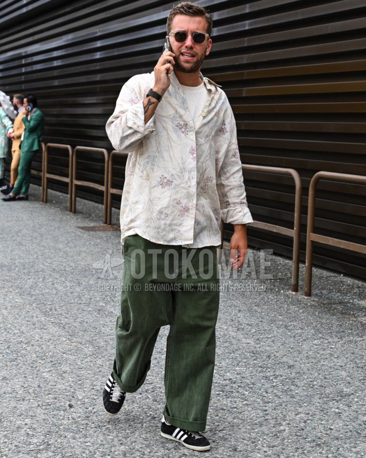 Men's spring, summer, and fall coordinate and outfit with plain black sunglasses, white top/inner shirt, plain white t-shirt, olive green plain wide-leg pants, and black low-cut Adidas sneakers.