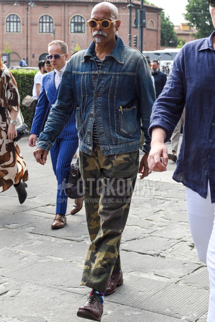 Men's spring, summer, and fall coordination and outfit with plain yellow/black sunglasses, plain blue shirt, plain navy/white t-shirt, wide green camouflage pants, multi-colored plain socks, and brown brogue shoes leather shoes.