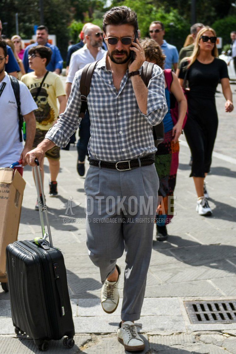 Men's spring/summer outfit and outfit with plain beige sunglasses, gray/white checked shirt, plain black leather belt, plain mesh belt, plain gray slacks, plain pleated pants, white low-cut sneakers, and plain black suitcase.
