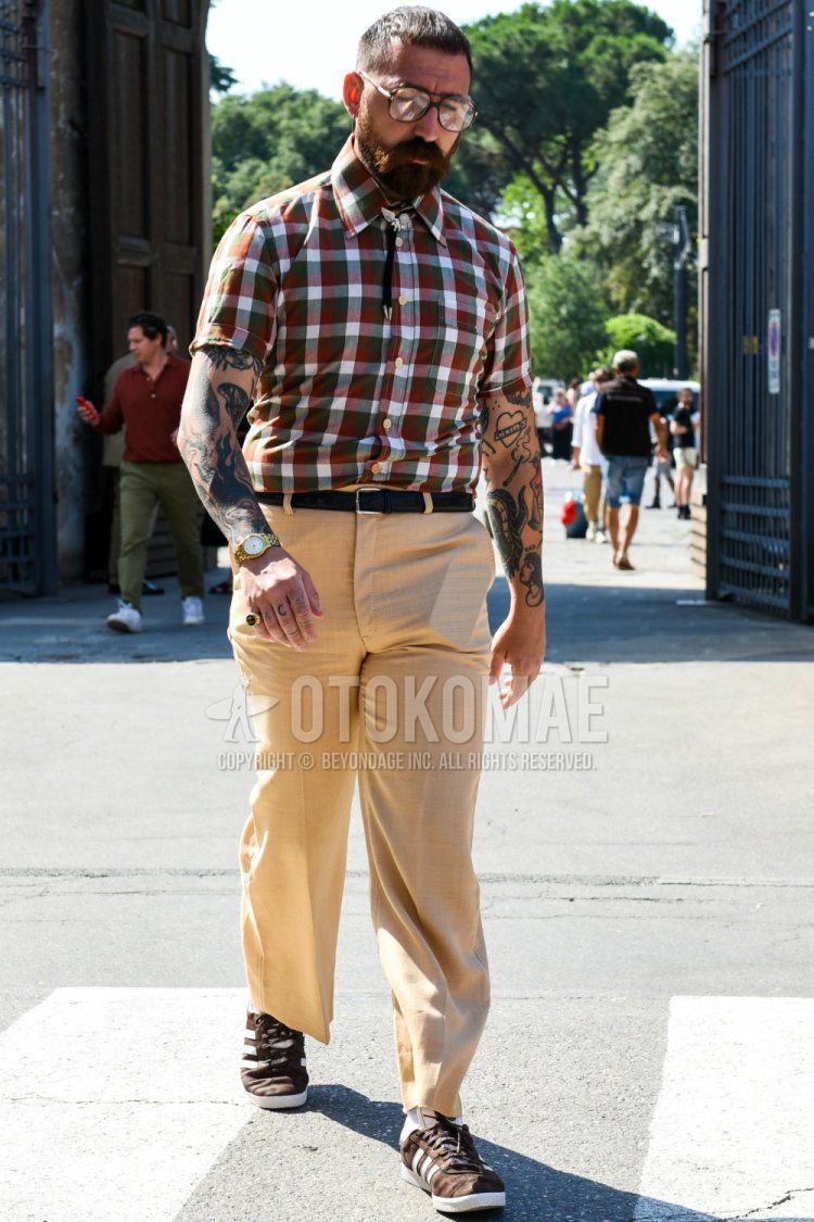Men's spring/summer coordinate and outfit with brown tortoiseshell glasses, short-sleeved multi-colored checked shirt, plain black leather belt, plain beige slacks, plain white socks, and brown low-cut Adidas sneakers.