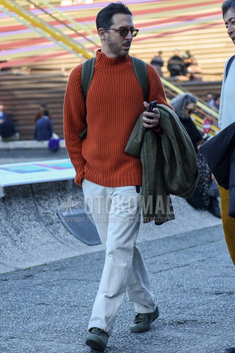 Men's spring and fall coordinate and outfit with brown tortoiseshell sunglasses, plain orange sweater, plain white cotton pants, and gray low-cut sneakers.