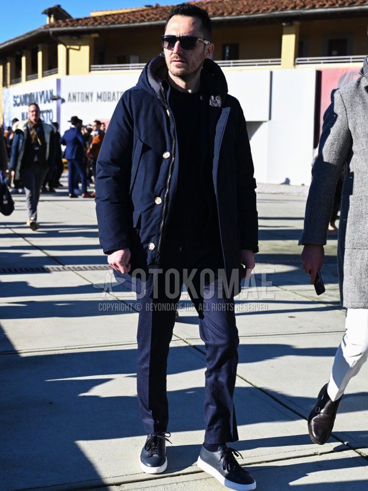Men's fall/winter outfit and outfit with plain navy down jacket, plain navy hooded coat, plain black sweatshirt, plain navy slacks, plain navy socks, and navy low-cut sneakers.