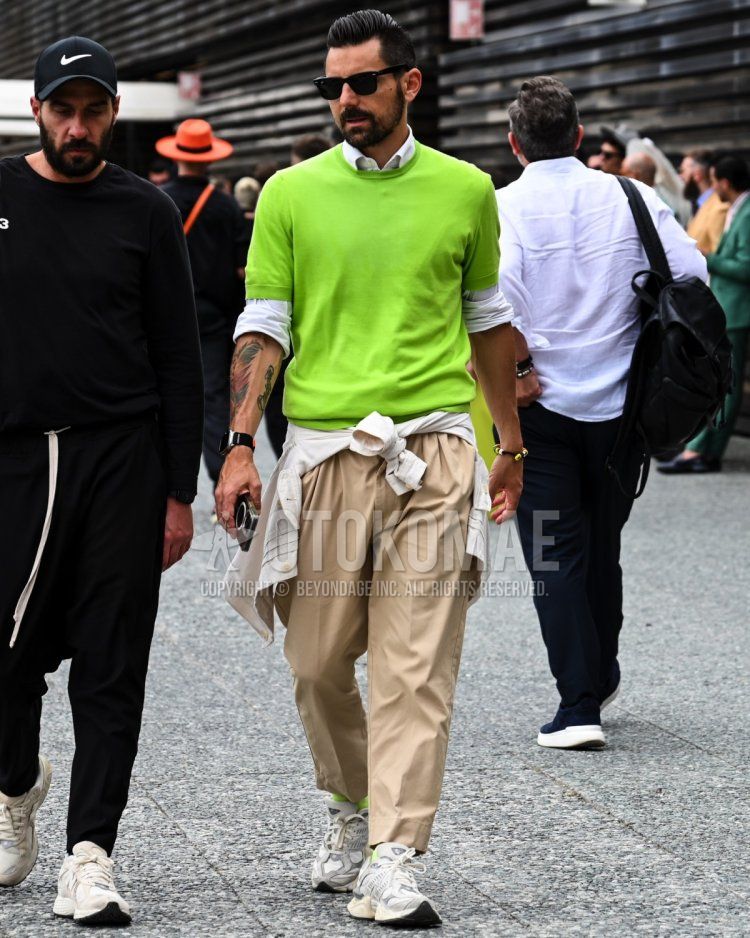 Men's spring, summer, and fall coordinate and outfit with solid black sunglasses, solid green sweater, solid white shirt, solid beige chinos, and white low-cut sneakers.
