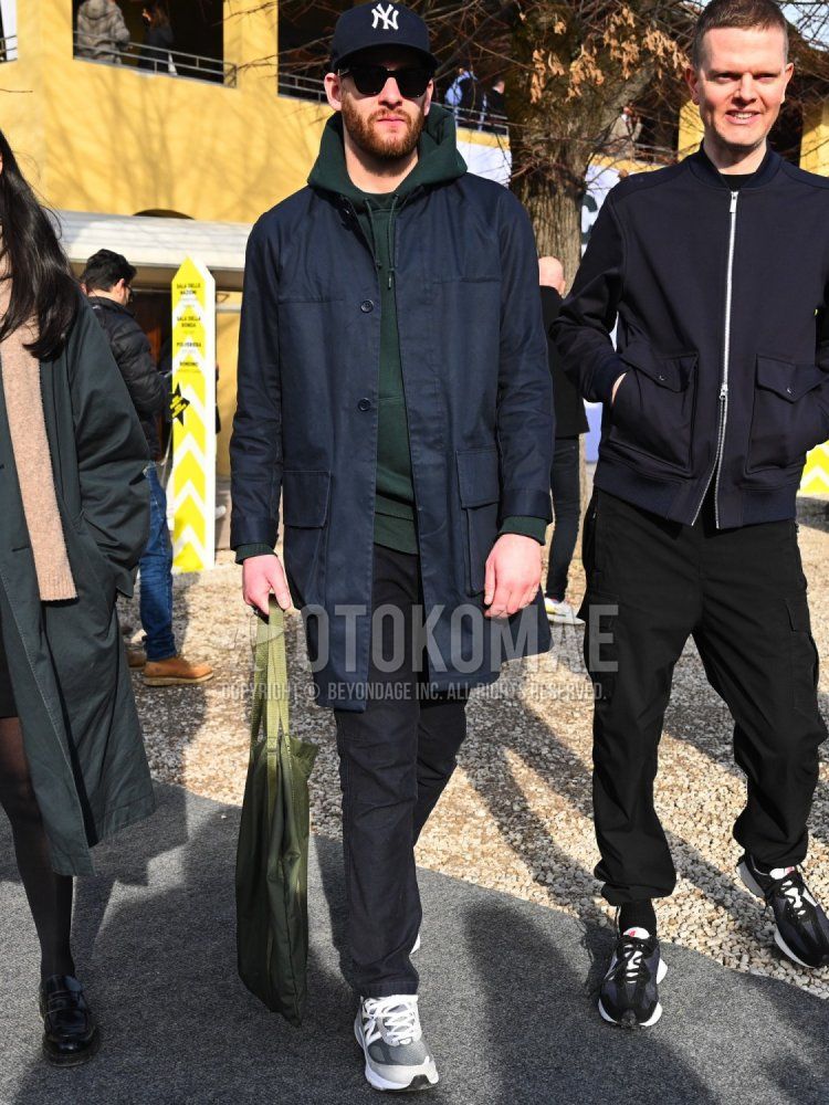 Men's fall/winter coordinate and outfit with navy decalogo baseball cap, solid black sunglasses, solid navy stainless steel collar coat, solid green hoodie, solid black cotton pants, gray low-cut sneakers, and solid olive green tote bag.