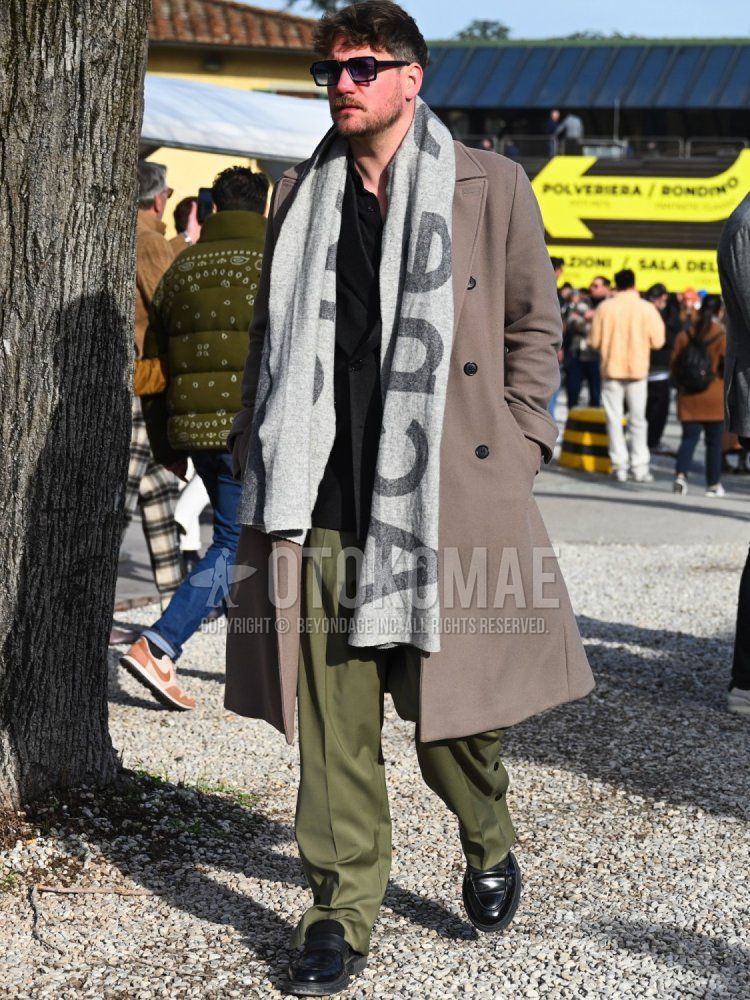Men's fall/winter outfit with plain black sunglasses, green deca logo scarf/stall, plain brown Ulster coat, plain black tailored jacket, plain black shirt, plain olive green slacks, black coin loafer leather shoes.