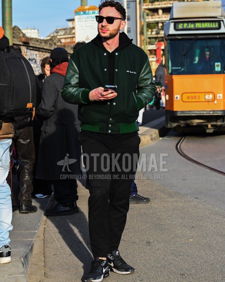 Men's fall/winter coordinate and outfit with plain black sunglasses, plain green stadium jacket, plain black hoodie, plain black cotton pants, and Nike Air Max 90 black low-cut sneakers.