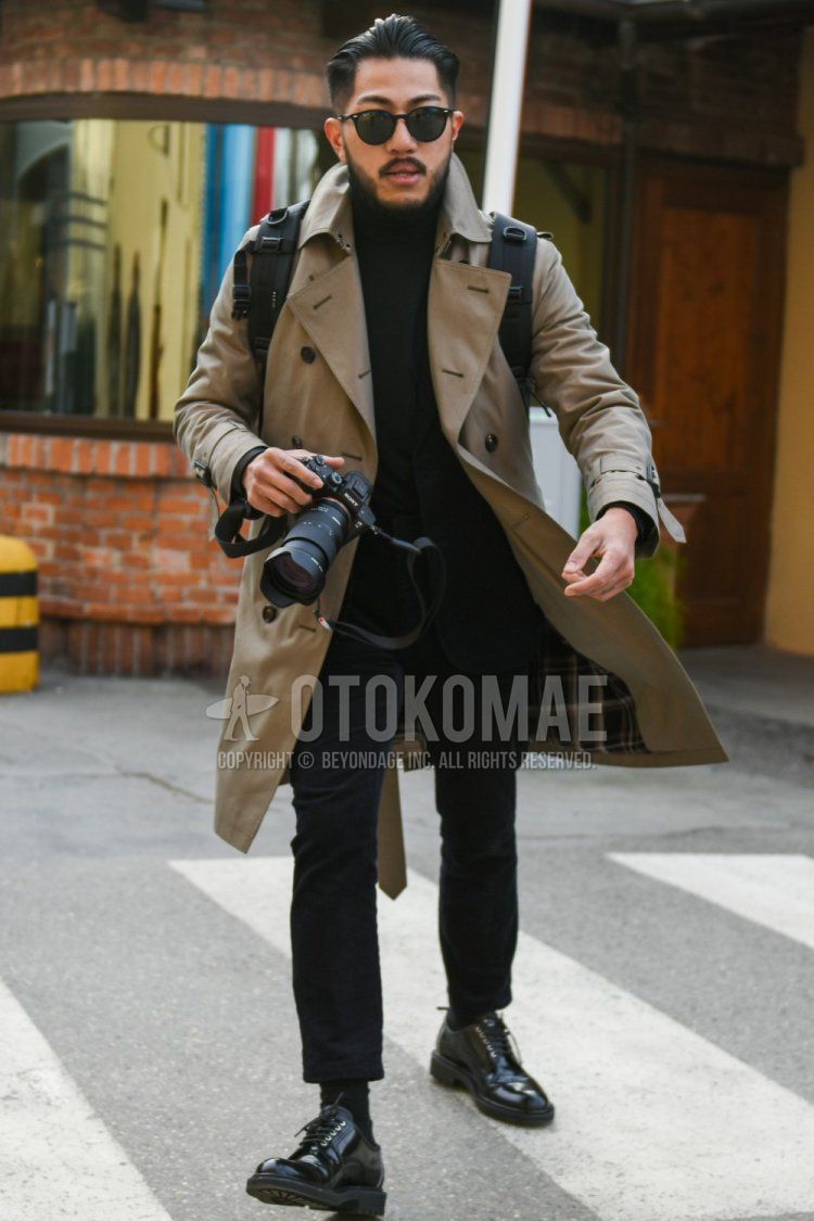 Men's fall/winter outfit with Boston Ray-Ban solid black sunglasses, solid beige trench coat, solid black turtleneck knit, solid black slacks, solid black ankle pants, solid black socks, solid black plain toe leather shoes, and solid black backpack.