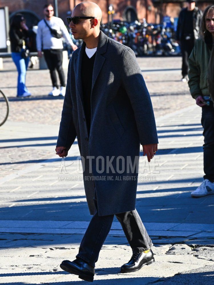 Men's fall/winter outfit with plain black sunglasses, plain gray chester coat, plain white t-shirt, plain black sweater, plain black denim/jeans, olive green checked socks, and black u-tip leather shoes.