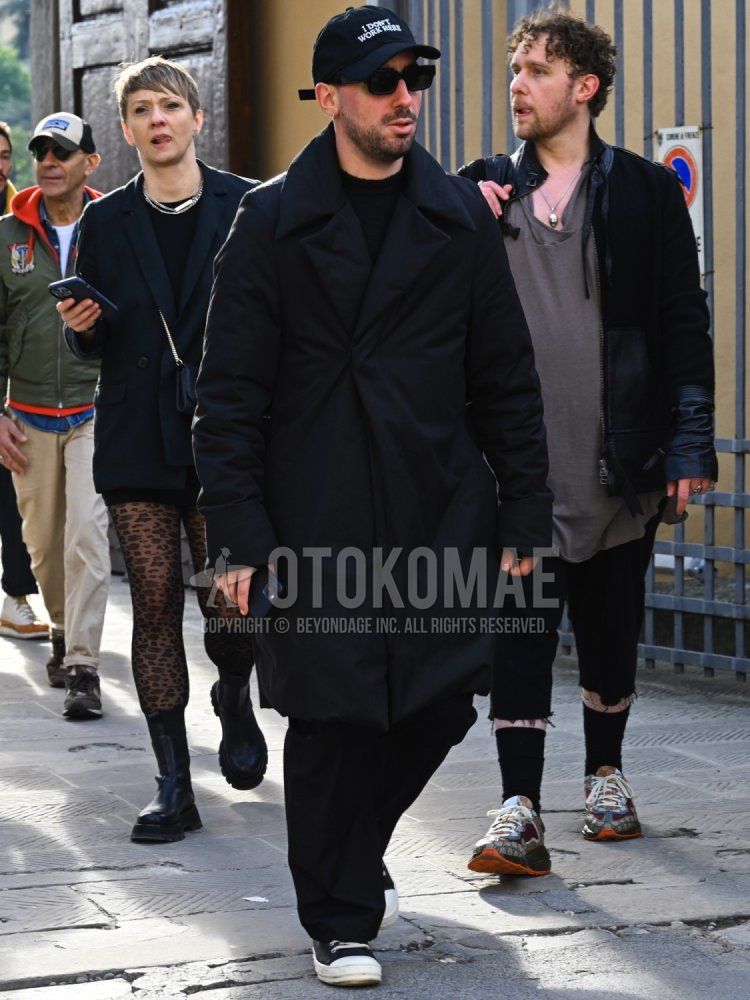 Men's fall/winter coordinate and outfit with black big logo baseball cap, solid black sunglasses, solid black outerwear, solid black sweater, solid black slacks, and black low-cut sneakers.