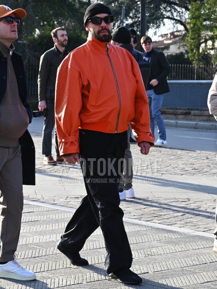 Men's fall/winter coordinate and outfit with solid black knit cap, solid black sunglasses, solid orange outerwear, and solid black cargo pants.