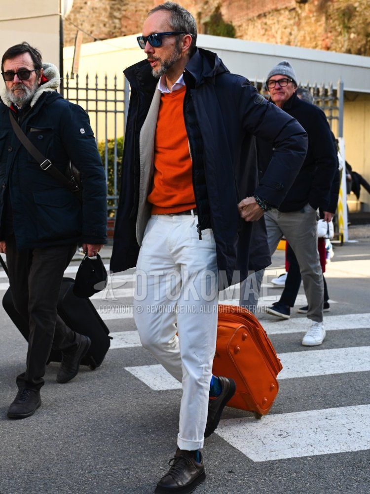 Solid black sunglasses, solid navy windbreaker, solid orange sweater, solid white shirt, solid black casual vest, solid black leather belt, solid white cotton pants, navy socks, brown plain toe leather shoes, solid orange suitcase. Men's fall/winter outfits/coordinates.