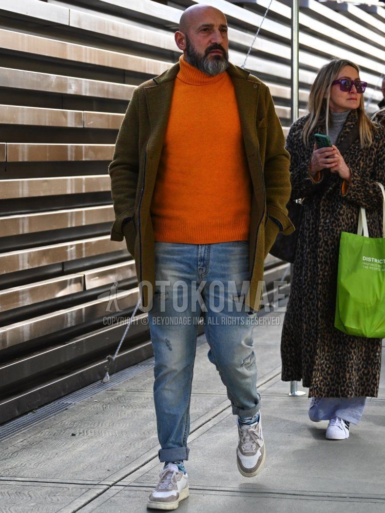 Men's winter/autumn coordinate and outfit with olive green solid color chester coat, orange solid color turtleneck knit, blue solid color damaged jeans, blue socks socks, and Autry gray low-cut sneakers.