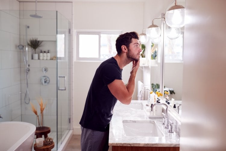 Man Wearing Pyjamas Standing At Sink Putting On Moisturizer In Bathroom