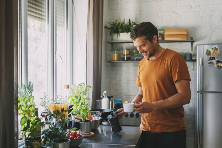 Handsome Young Man Holding a Coffee Maker and a Mug over a Kitchen Counter