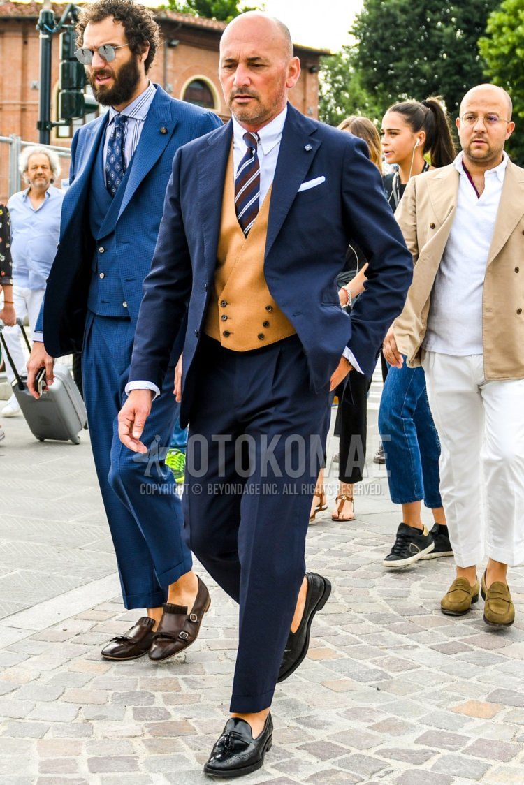Men's spring and autumn coordinate and outfit with plain beige gilet, plain white shirt, black tassel loafer leather shoes, plain navy suit by Lardini, and striped tie.