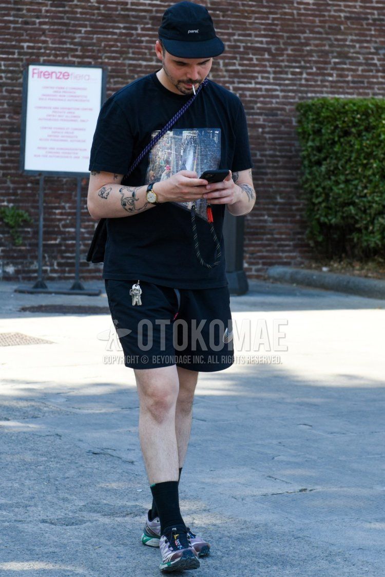 Men's summer coordinate and outfit with black one-point jet cap, black graphic t-shirt, Nike black one-point shorts, plain black socks, and Salomon black low-cut sneakers.