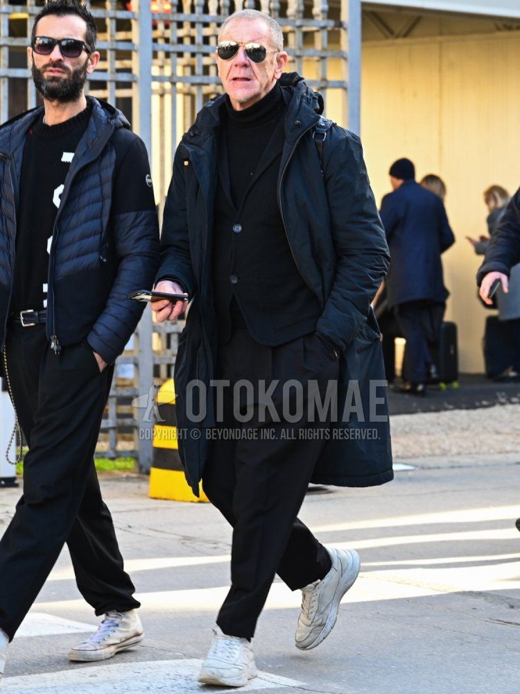 Men's fall/winter coordinate and outfit with plain black hooded coat, plain black tailored jacket, plain black turtleneck knit, plain black pleated pants, and white low-cut sneakers.
